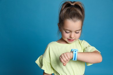 Little girl with smart watch on light blue background, space for text