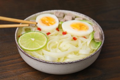 Photo of Bowl of delicious rice noodle soup with meat and egg on wooden table, closeup
