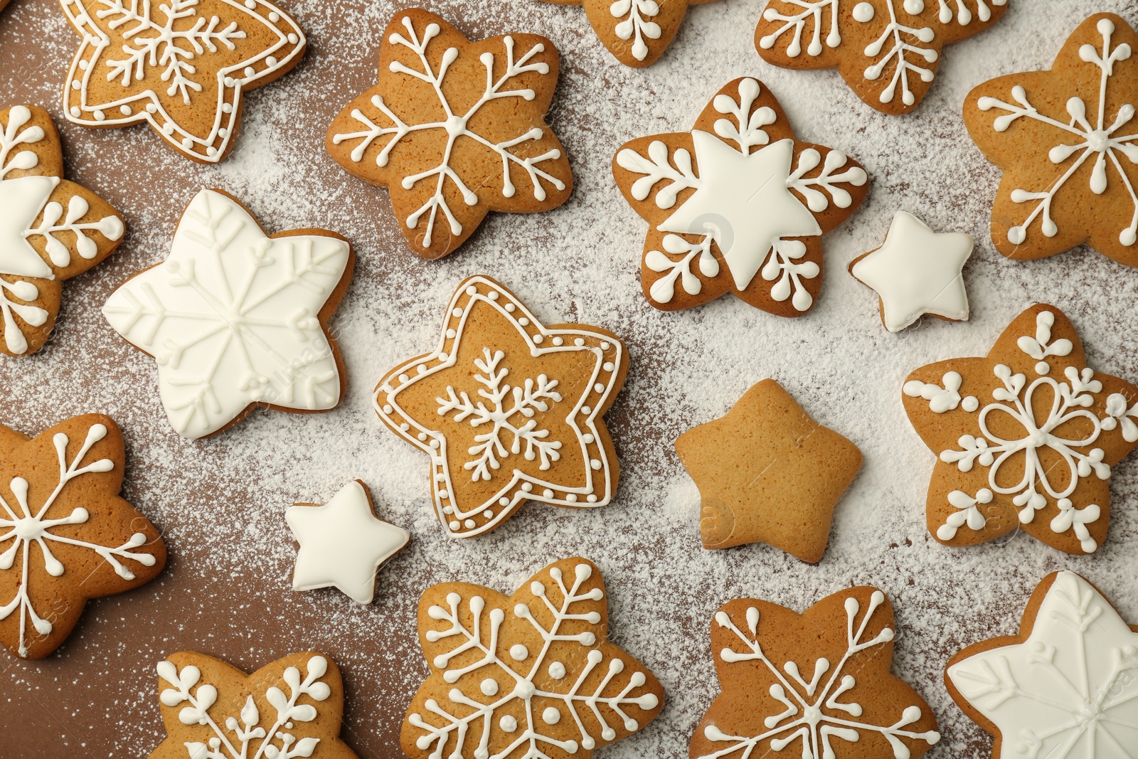 Photo of Tasty Christmas cookies with icing and powdered sugar on brown background, flat lay