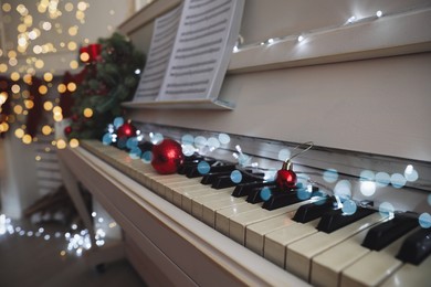 Photo of Red baubles and fairy lights on piano keys indoors, closeup. Christmas music