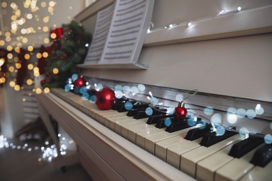 Red baubles and fairy lights on piano keys indoors, closeup. Christmas music