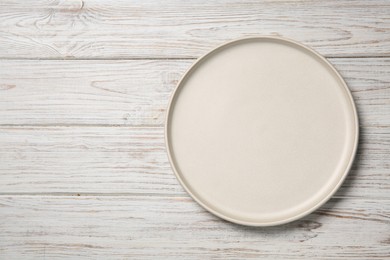 Photo of One white ceramic plate on light wooden table, top view. Space for text