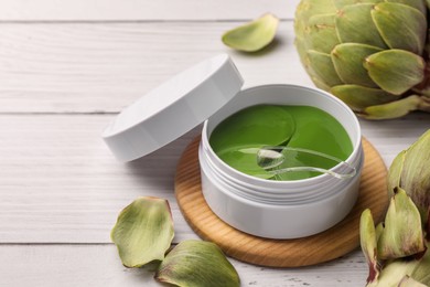 Package of under eye patches and artichokes on white wooden table, closeup with space for text. Cosmetic product