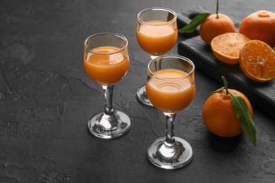 Photo of Tasty tangerine liqueur in glasses and fresh citrus fruits on black textured table. Space for text