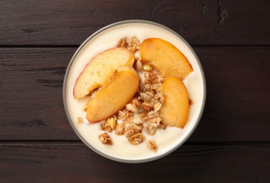 Photo of Tasty peach yogurt with granola and pieces of fruits in bowl on wooden table, top view