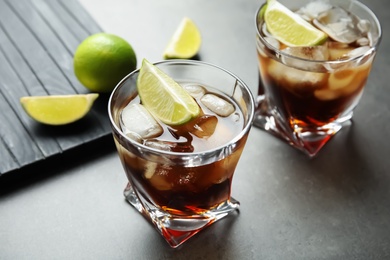 Photo of Glasses of cocktail with cola, ice and cut lime on grey background