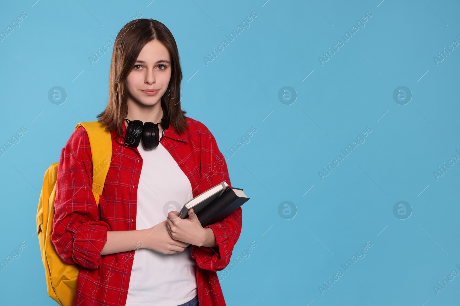 Photo of Portrait of beautiful teenage girl with books on light blue background. Space for text