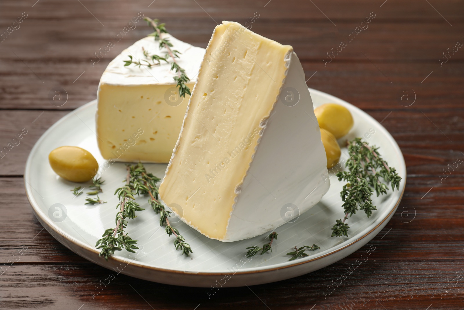 Photo of Plate with pieces of tasty camembert cheese, olives and rosemary on wooden table, closeup