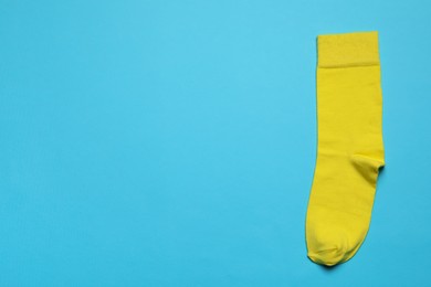 Photo of New yellow sock on light blue background, top view. Space for text