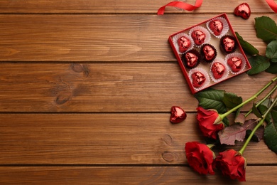 Heart shaped chocolate candies and bouquet on wooden table, flat lay. Space for text