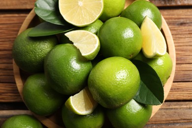 Photo of Fresh limes and green leaves on wooden table, top view