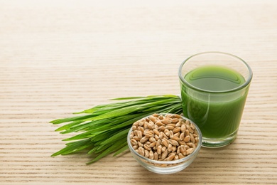 Photo of Shot glass of wheat grass juice, bowl with grains and sprouts on wooden table, space for text