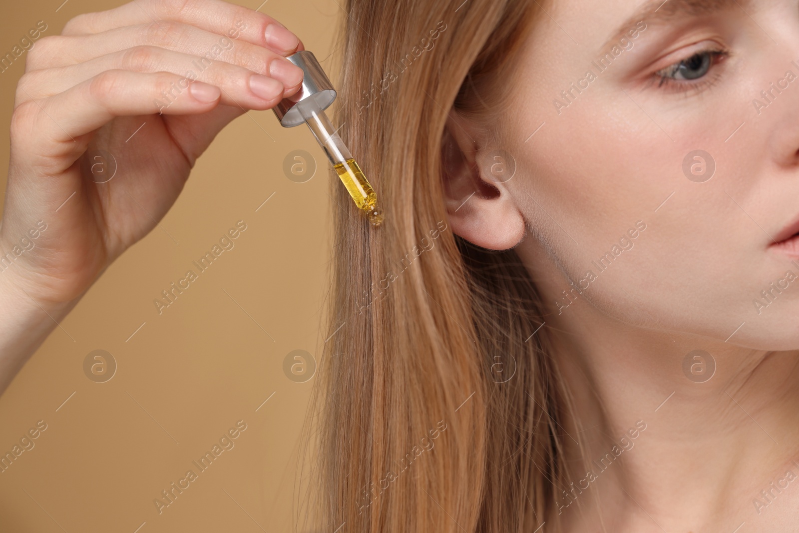 Photo of Woman applying essential oil onto hair on beige background, closeup