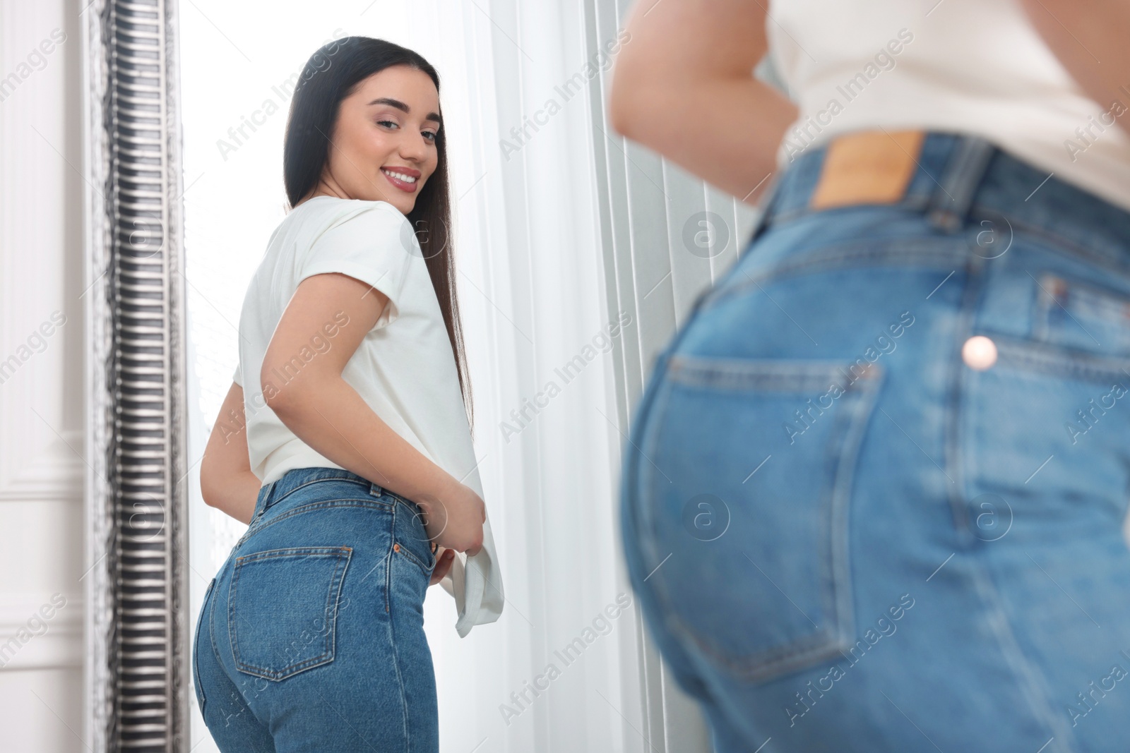Photo of Young woman in stylish jeans near mirror indoors