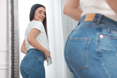 Young woman in stylish jeans near mirror indoors