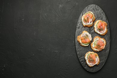 Tasty canapes with salmon, cucumber, radish and cream cheese on black table, top view. Space for text