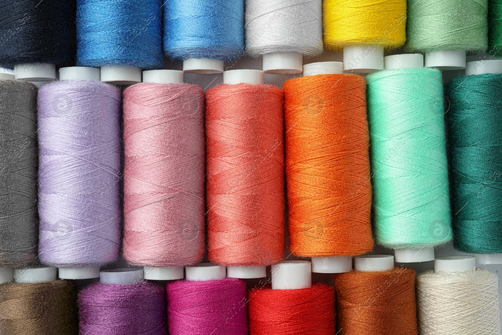 Photo of Set of different colorful sewing threads as background, top view