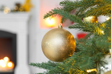 Photo of Beautiful golden Christmas ball hanging on fir tree branch against blurred background, closeup