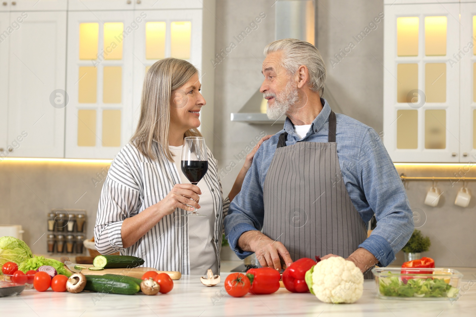 Photo of Happy senior couple cooking together in kitchen. Woman with glass of wine near her husband