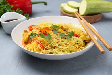 Photo of Stir-fry. Delicious cooked noodles with chicken and vegetables in bowl served on gray textured table, closeup