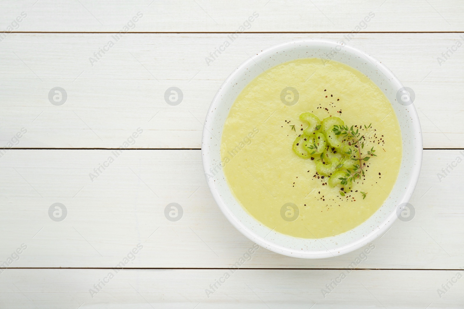 Photo of Bowl of delicious celery soup on white wooden table, top view. Space for text