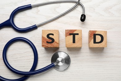 Abbreviation STD made with cubes near stethoscope on white wooden table, flat lay