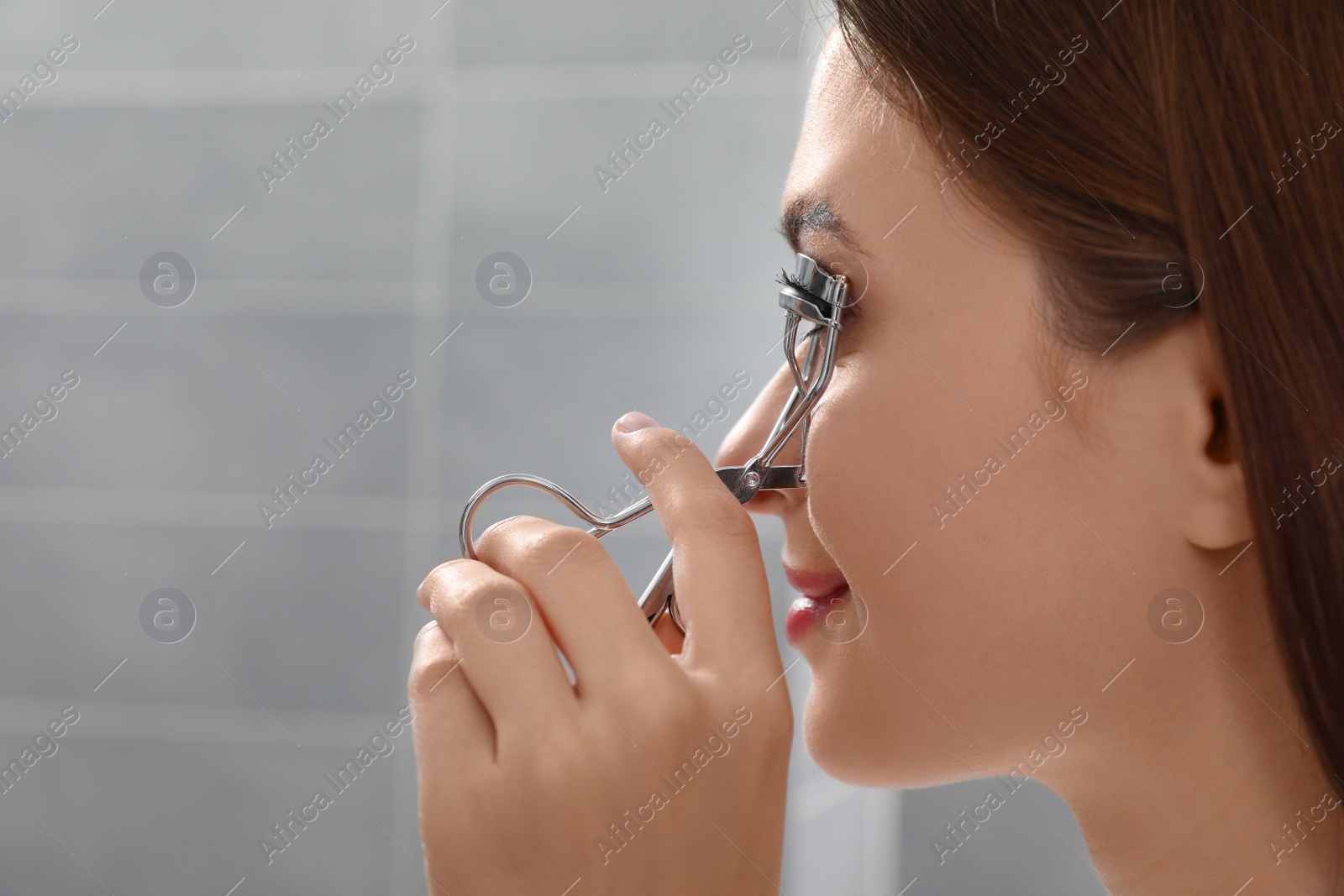 Photo of Young woman using eyelash curler indoors, closeup. Space for text