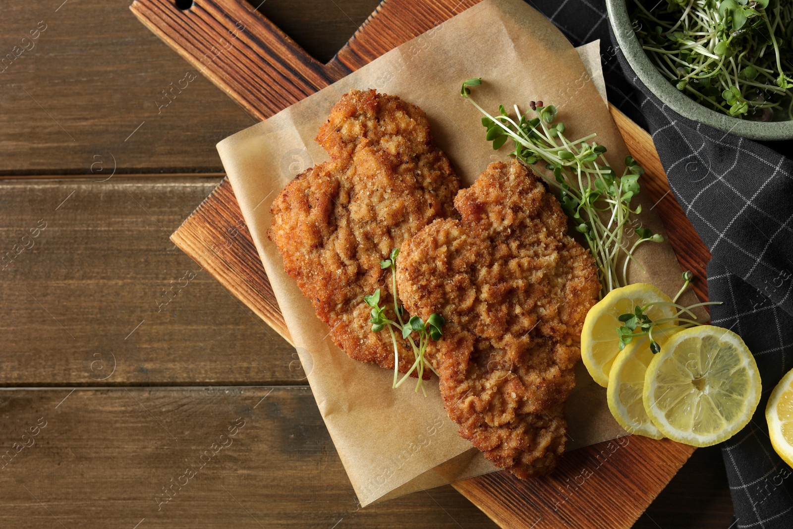 Photo of Tasty schnitzels served with lemon and microgreens on wooden table, flat lay. Space for text