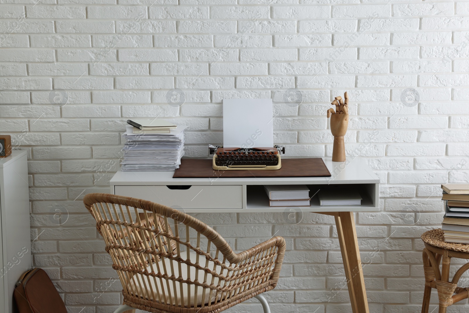 Photo of Comfortable writer's workplace with typewriter on desk near white brick wall