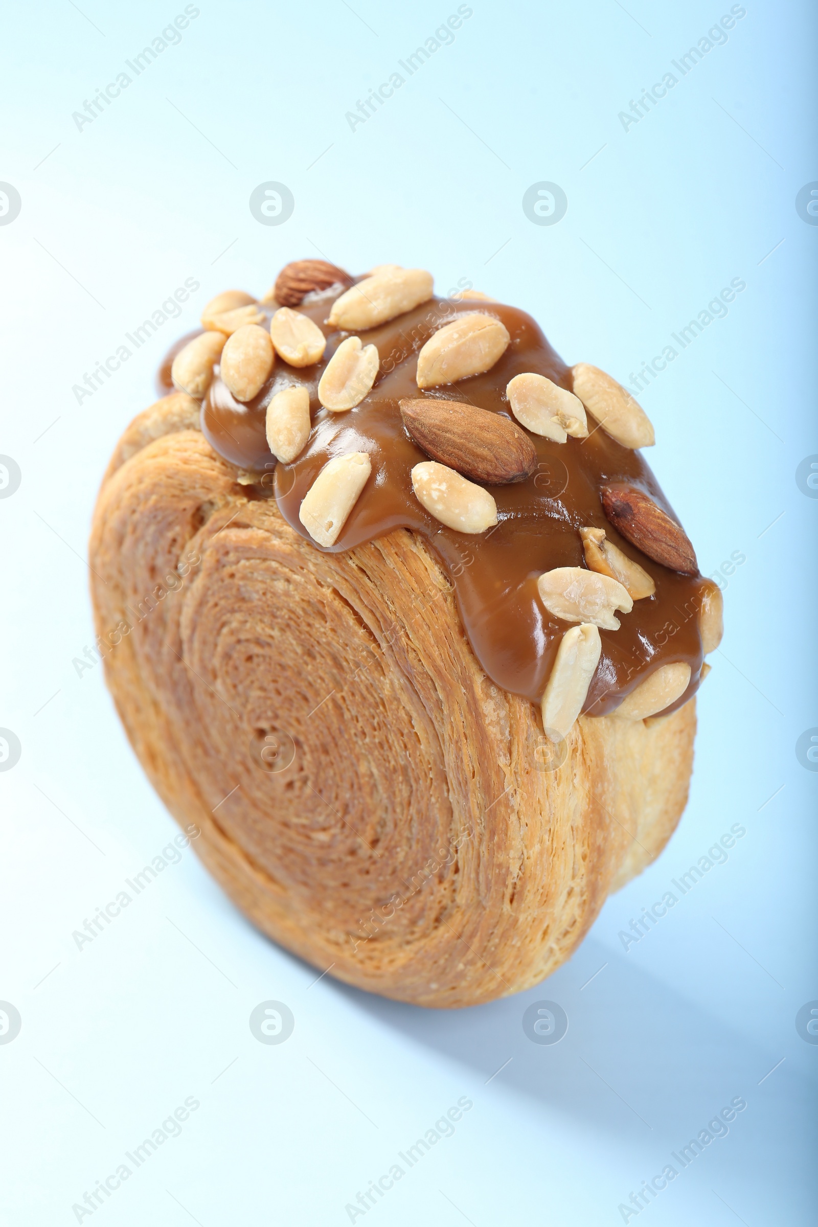 Photo of One supreme croissant with chocolate paste and nuts on light blue background, closeup. Tasty puff pastry