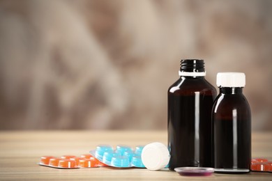 Bottles of syrup, dosing spoon and cough drops on wooden table. Space for text