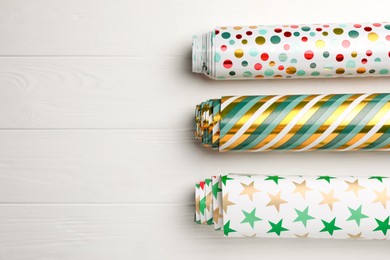 Photo of Different colorful wrapping paper rolls on white wooden table, flat lay. Space for text