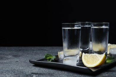 Photo of Shot glasses of vodka with lemon slices, mint and ice on grey table. Space for text