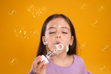 Photo of Little girl blowing soap bubbles on yellow background