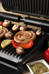 Photo of Electric grill with homemade sausages, mushrooms and bell pepper on table, closeup