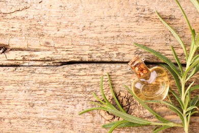 Aromatic essential oil in bottle and rosemary on wooden table, flat lay. Space for text