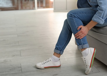 Photo of Young woman suffering from leg pain indoors, closeup with space for text