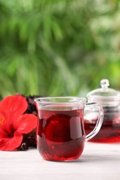 Glass cup of delicious hibiscus tea on white wooden table outdoors, space for text