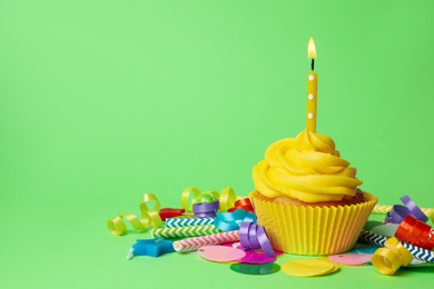 Delicious birthday cupcake with yellow cream and burning candle on green background. Space for text