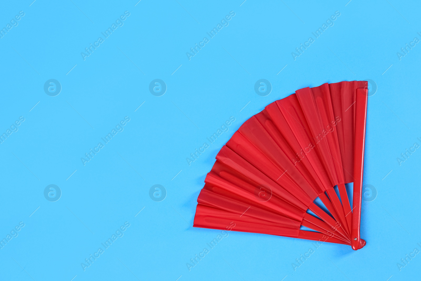 Photo of Red hand fan on light blue background, top view. Space for text