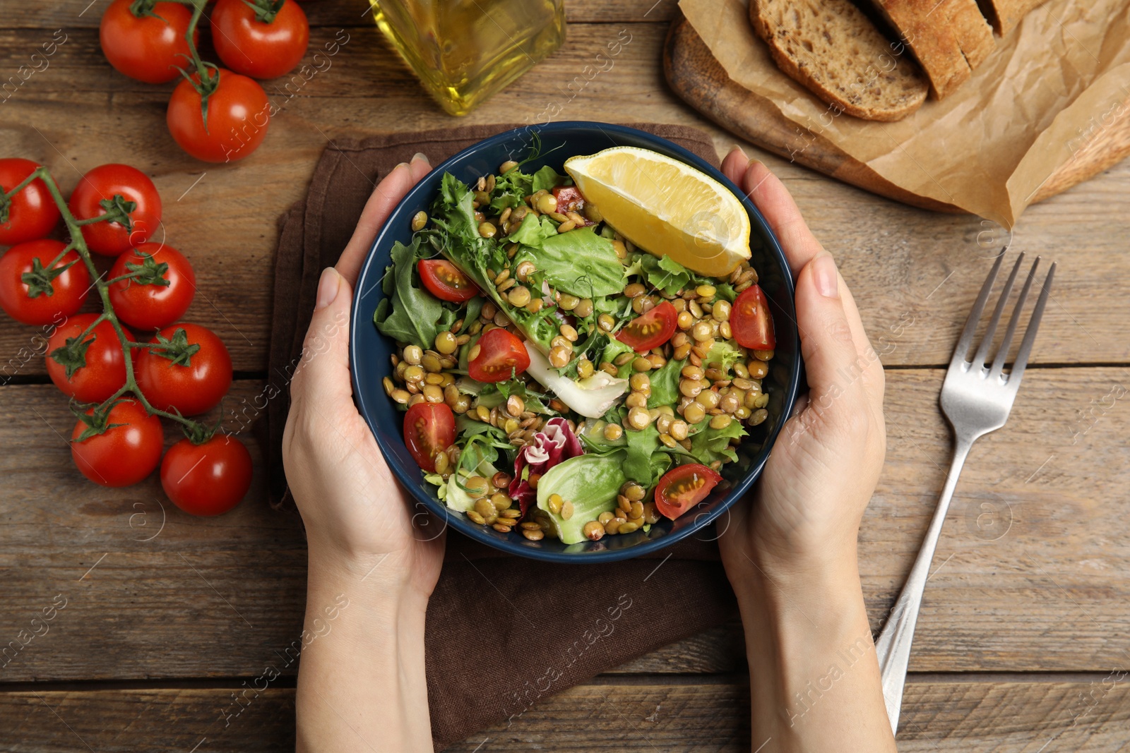 Photo of Woman holding bowl of delicious salad with lentils and vegetables at wooden table, top view