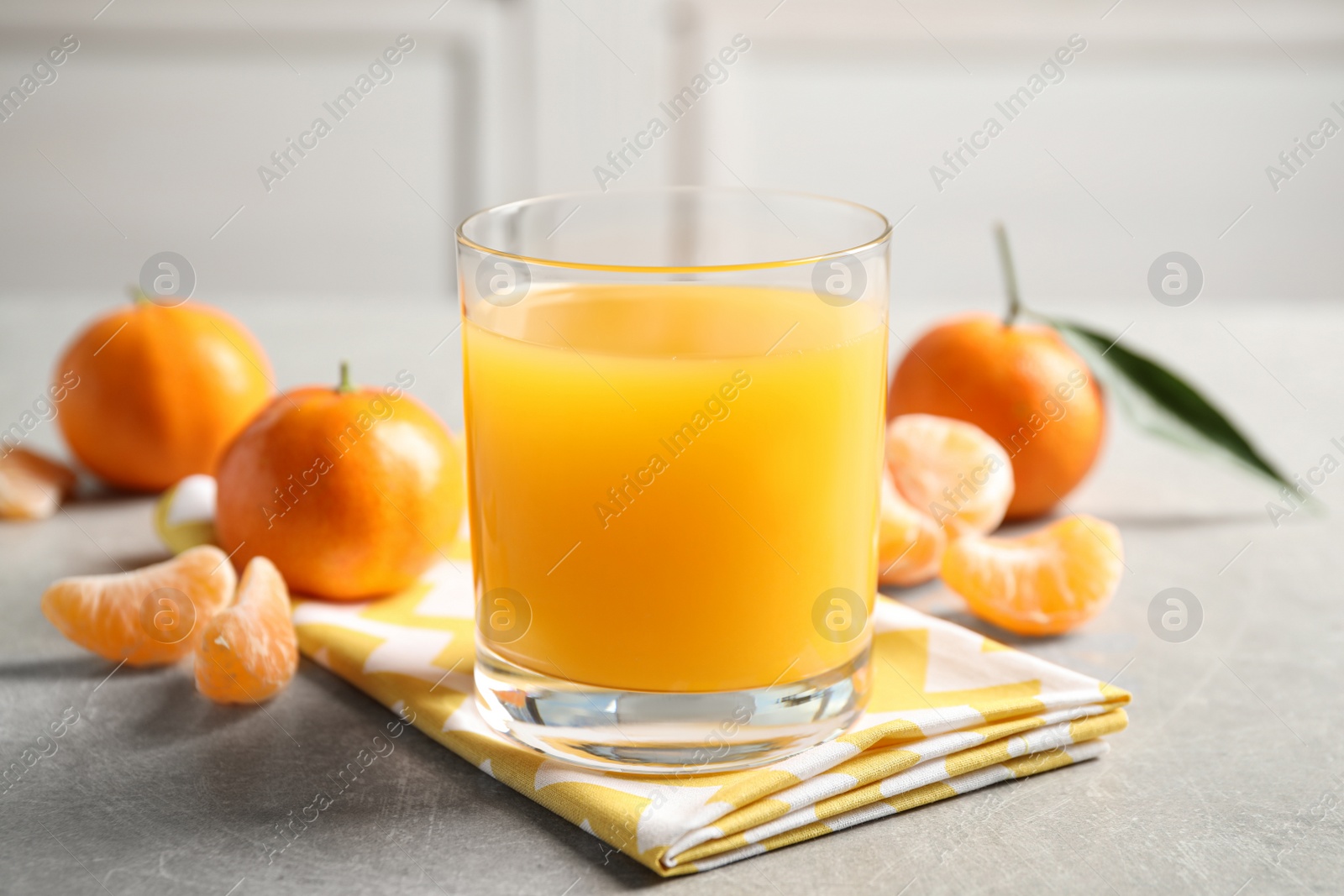 Photo of Glass of fresh tangerine juice and fruits on light grey table