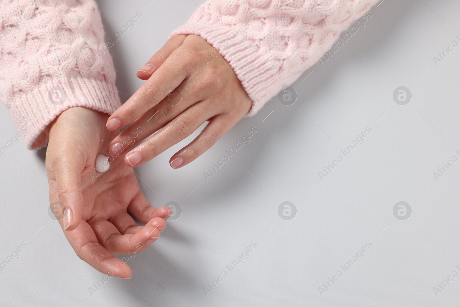 Photo of Woman applying cosmetic cream onto hand on light grey background, top view. Space for text