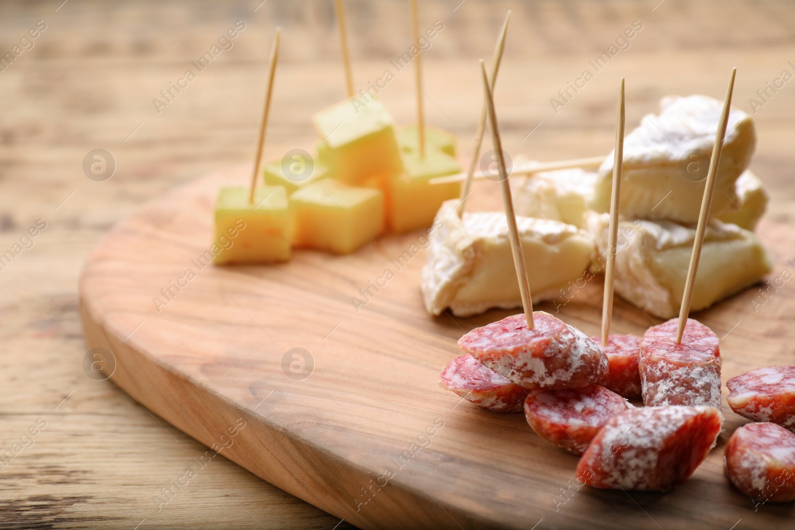 Photo of Toothpick appetizers. Pieces of sausage and cheese on wooden table, closeup view with space for text