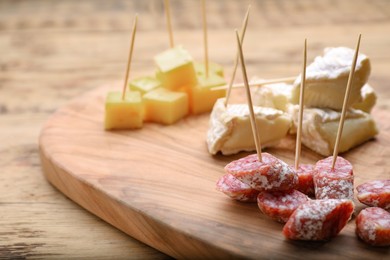 Photo of Toothpick appetizers. Pieces of sausage and cheese on wooden table, closeup view with space for text