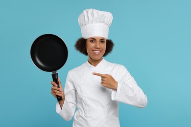 Photo of Happy female chef in uniform holding frying pan on light blue background