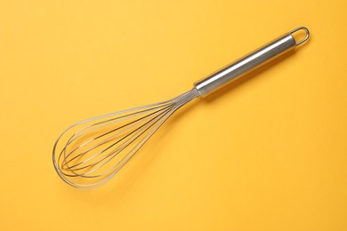 Photo of Metal whisk on yellow background, top view. Kitchen tool
