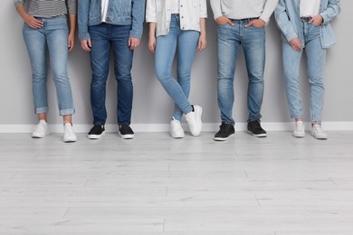 Group of people in stylish jeans near light grey wall indoors, closeup