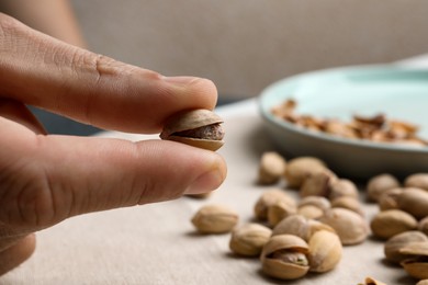 Photo of Woman holding tasty roasted pistachio nut at table, closeup. Space for text