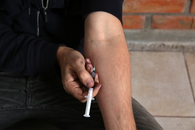 Photo of Male drug addict making injection near brick wall, closeup of hands